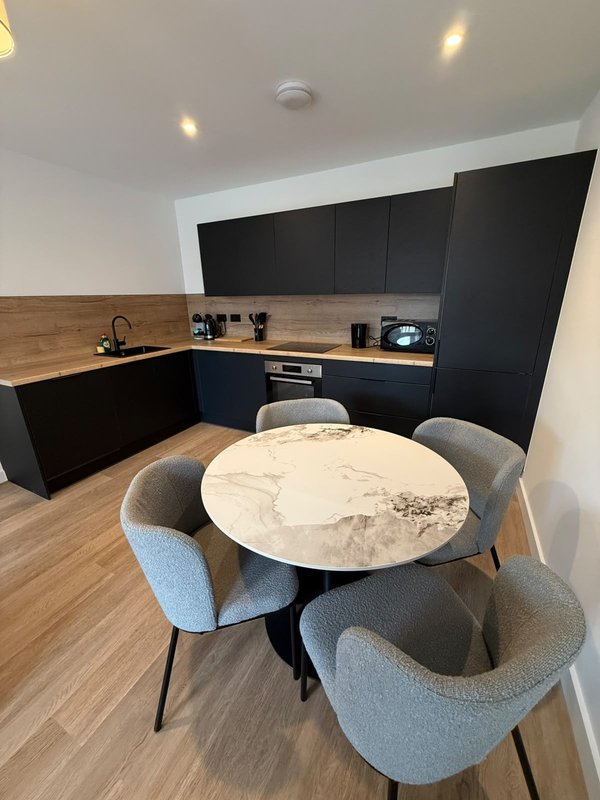 Modern open-plan kitchen and dining area with black cabinetry, round marble table, and grey upholstered chairs