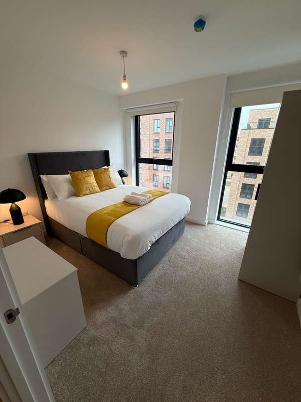 Bedroom with double bed, yellow cushions, pendant light, and windows overlooking street