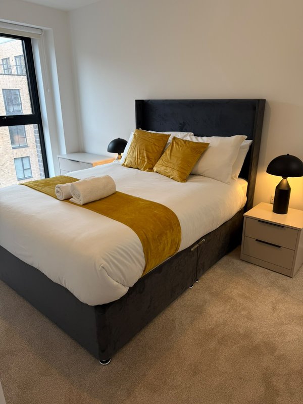 Modern bedroom with double bed, mustard-yellow accents, bedside table, and city view window