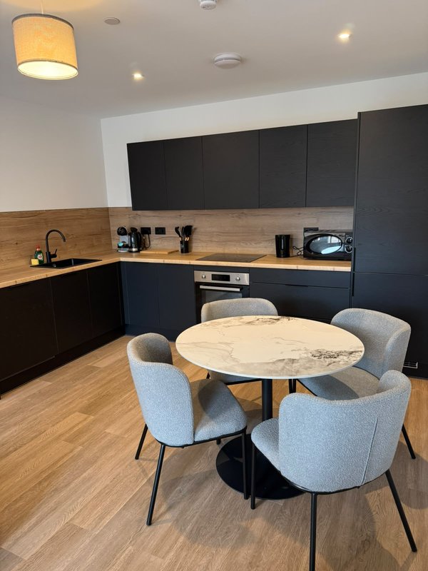 Modern kitchen with black cabinetry, wooden countertop, and round dining table with grey chairs