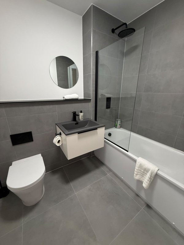 Modern bathroom with toilet, floating vanity, circular mirror, glass shower enclosure and bathtub