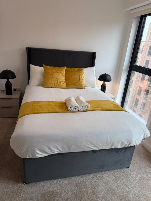 Modern bedroom with double bed, black headboard, gold pillows and bedding, black lamps, and city view window