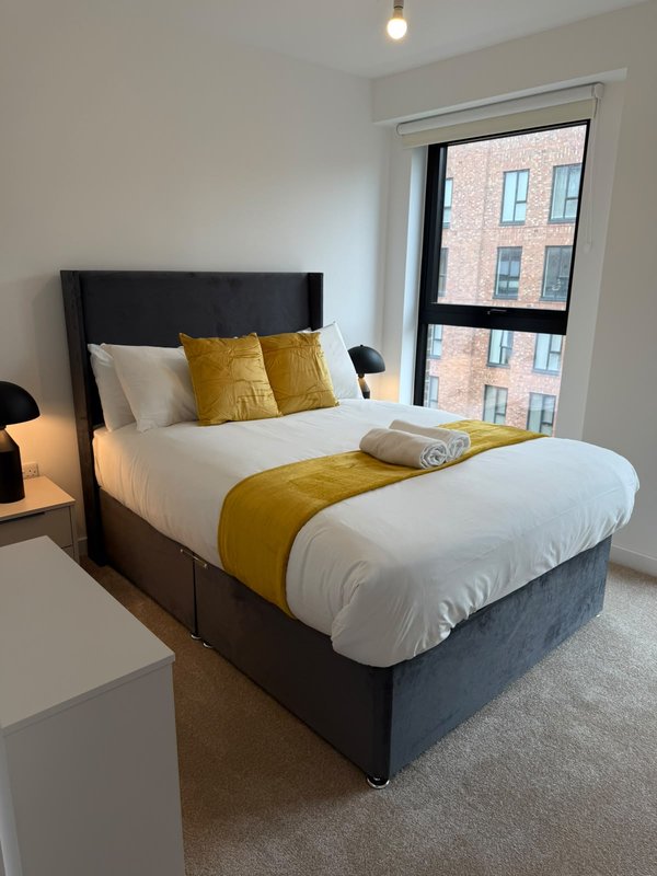 Modern bedroom with double bed, yellow cushions, white bedding and city view from window
