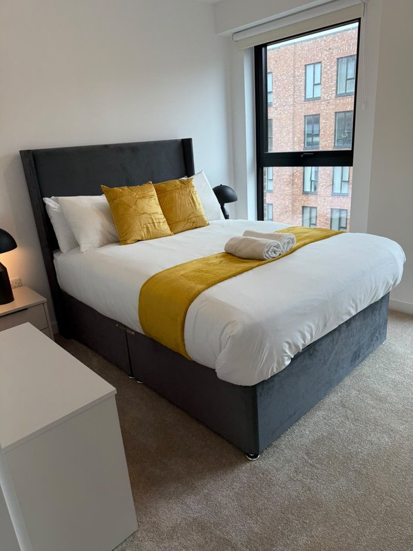 Modern bedroom with black upholstered bed, white bedding, gold cushions and throw, large window with city views
