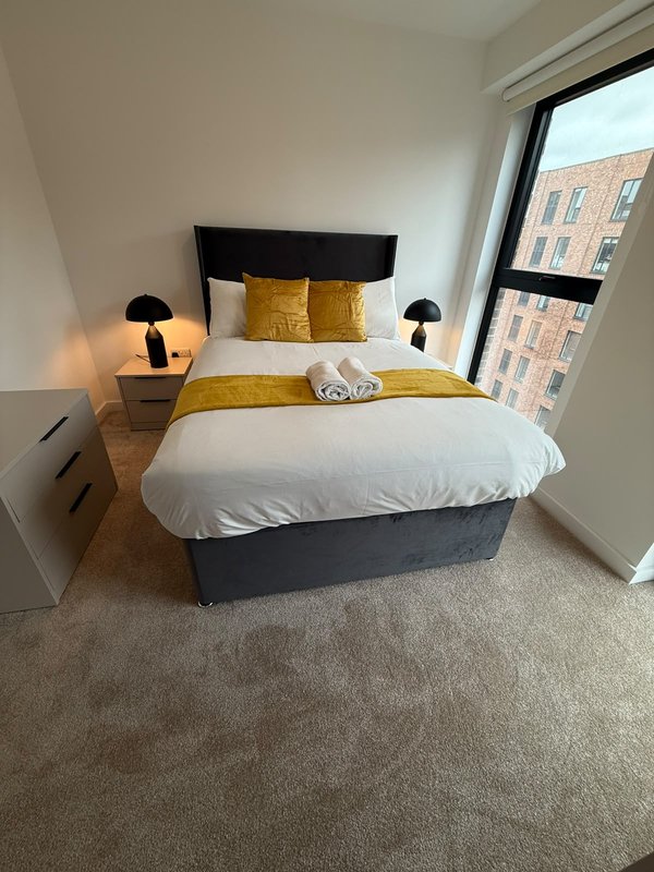 Modern bedroom with double bed, yellow cushions, bedside lamps and large window with city view