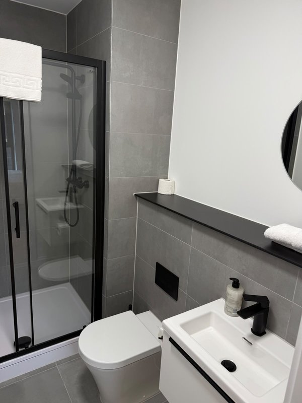 Modern bathroom with toilet, sink, shower enclosure and gray tile walls