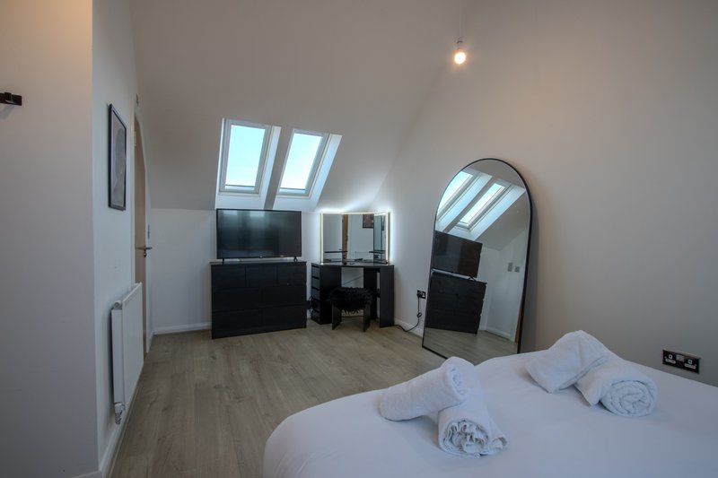Attic bedroom with sloped ceiling, skylight, double bed with white bedding and rolled towels, TV, mirror and wooden flooring