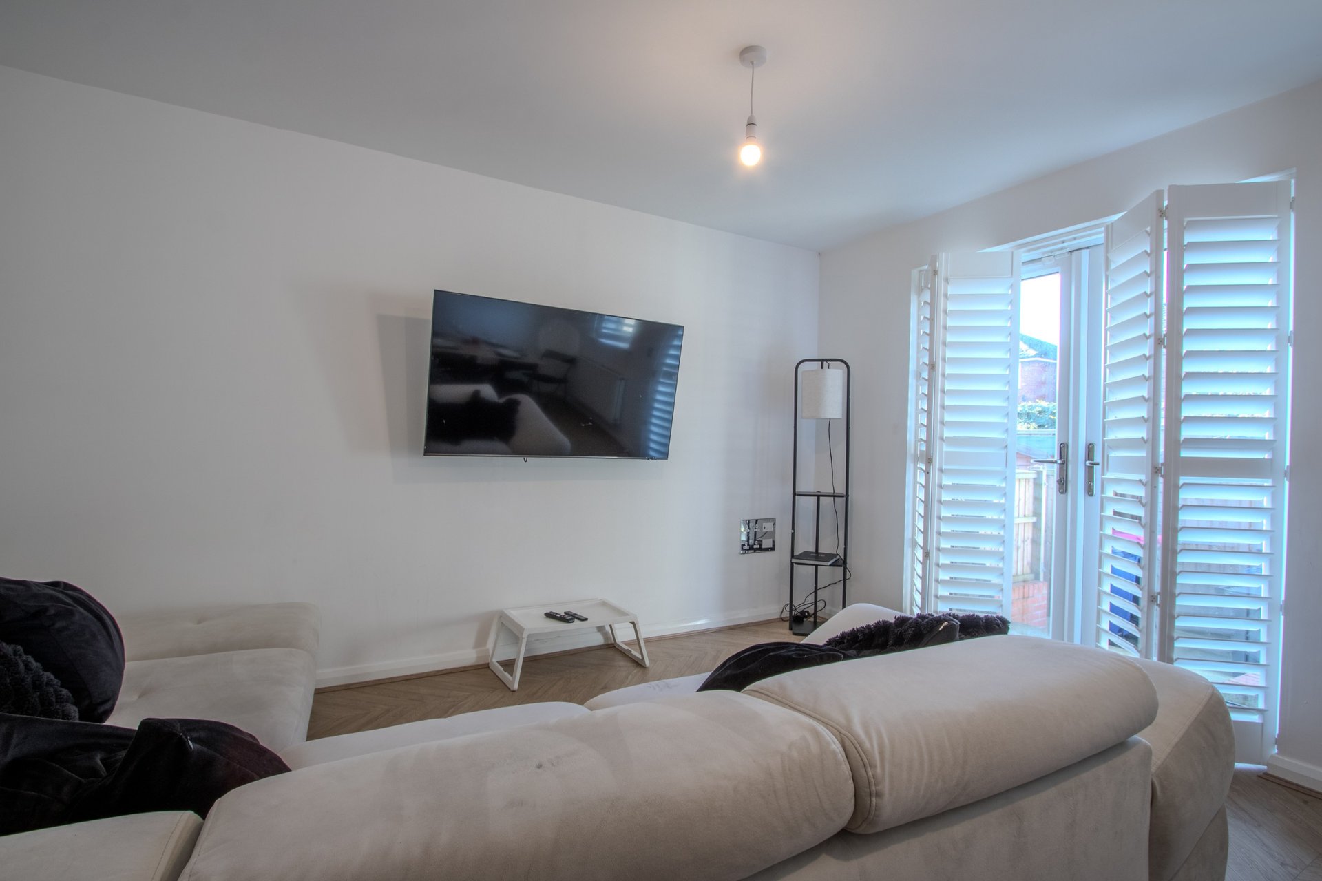 Bright bedroom with double bed, wall-mounted TV, lounge seating and glass door to balcony