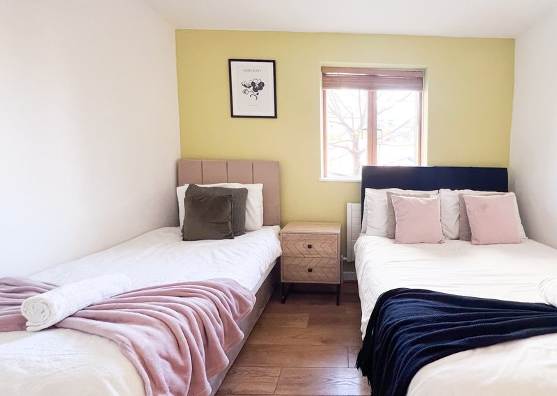 Bright bedroom with two single beds, yellow walls, wooden floor and window