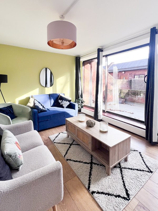Modern living room with blue sofa, grey armchairs, wooden coffee table and large sliding doors overlooking garden