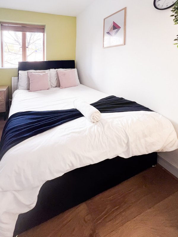 Bedroom with double bed, white bedding, blue throw, pink cushions and yellow accent wall