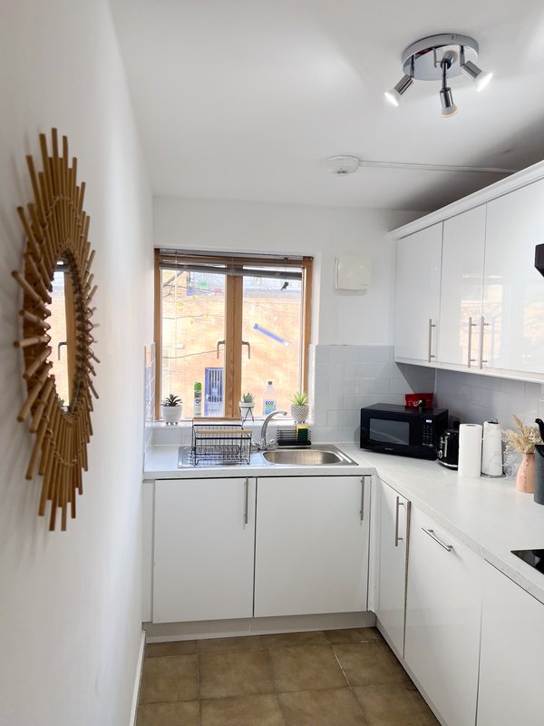 Modern white kitchen with compact layout, window overlooking street, gold wall art decoration