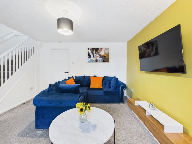Modern living room with blue sofa, yellow accent wall, TV, and white marble coffee table