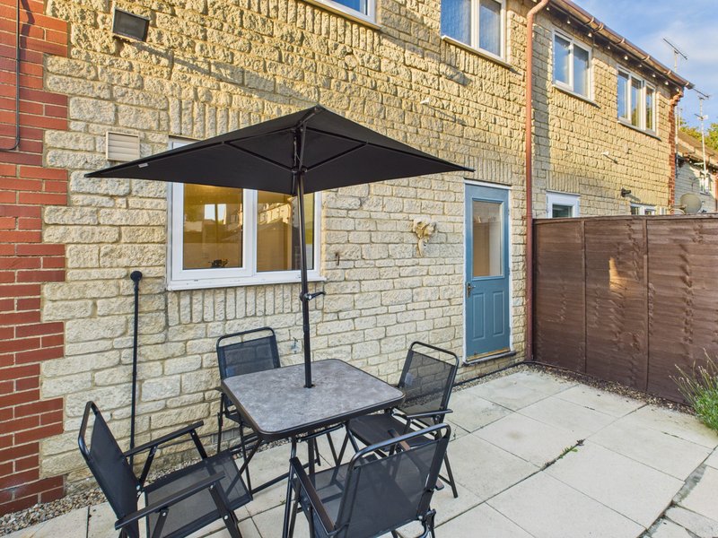 Patio area with dining table, chairs, black umbrella and brick property facade