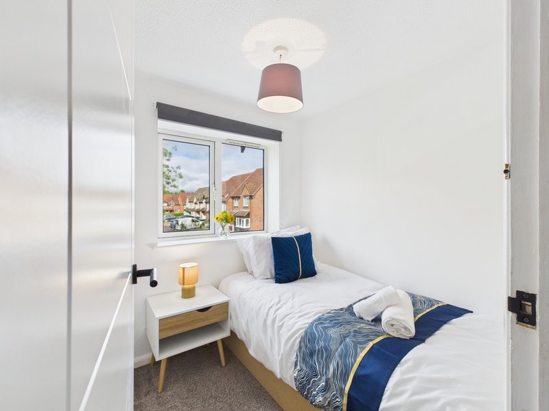 Compact bedroom with single bed, white nightstand, pendant lamp and window view