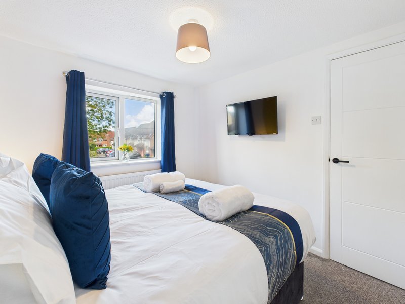 Bright bedroom with double bed, blue pillows, rolled towels, wall-mounted TV and mountain view through window