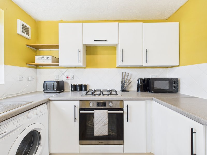 Compact kitchen with yellow walls, white cabinetry, cooktop, oven, and washing machine
