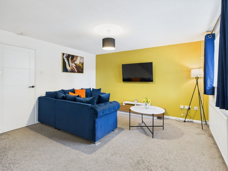 Living room with blue sofa, yellow accent wall, wall-mounted TV, coffee table and floor lamp