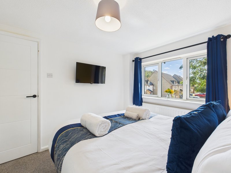 Modern bedroom with twin beds, white bedding, blue throws, wall-mounted TV and bright window view