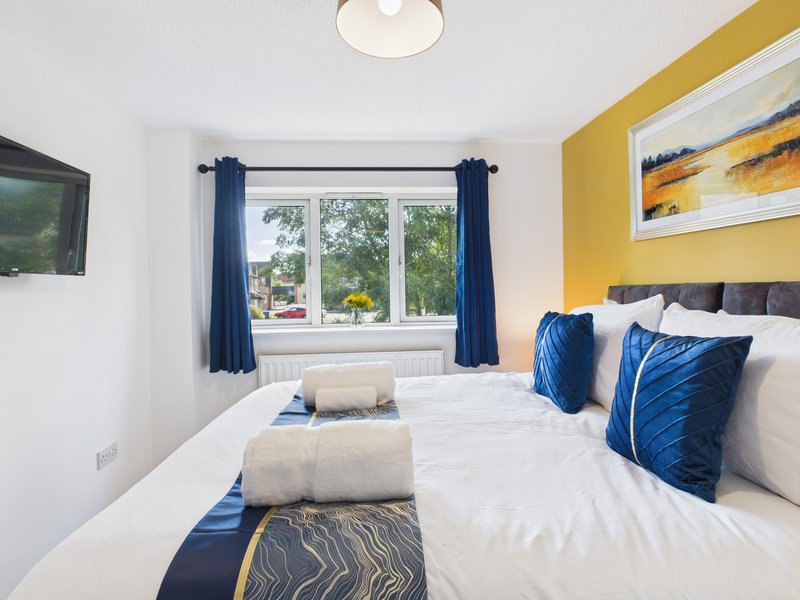 Bright bedroom with double bed, blue cushions, yellow accent wall, and garden view