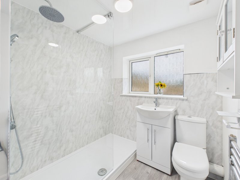 Modern bathroom with walk-in shower, marble tiles, white sink vanity, toilet, and window