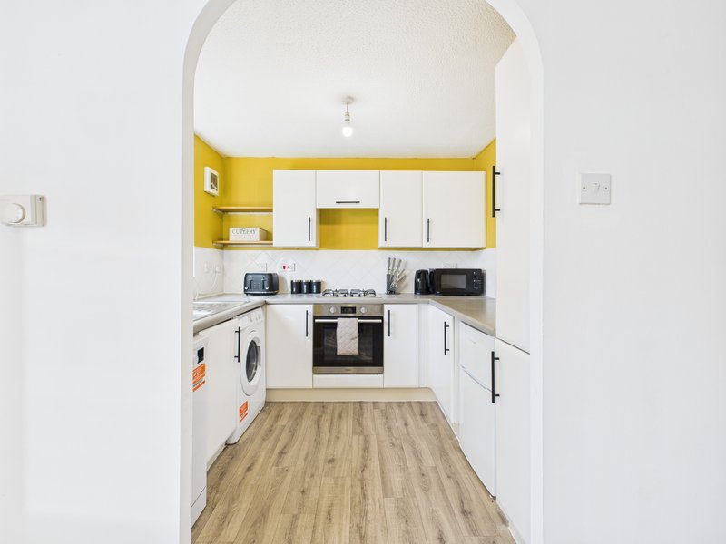 Modern kitchen with white cabinets, yellow accents, wooden flooring and built-in appliances