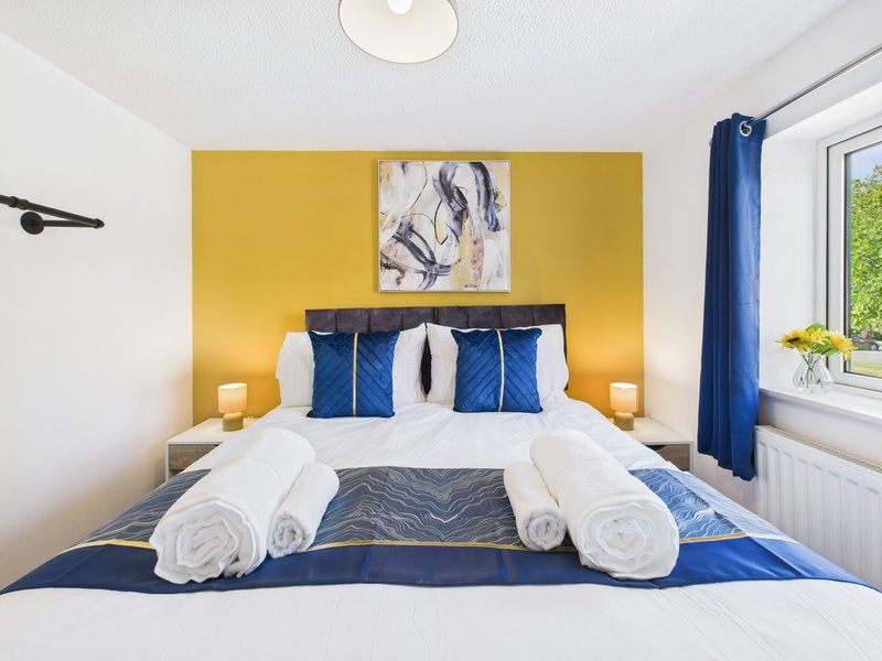 Modern bedroom with double bed, rolled white towels, blue pillows and yellow accent wall