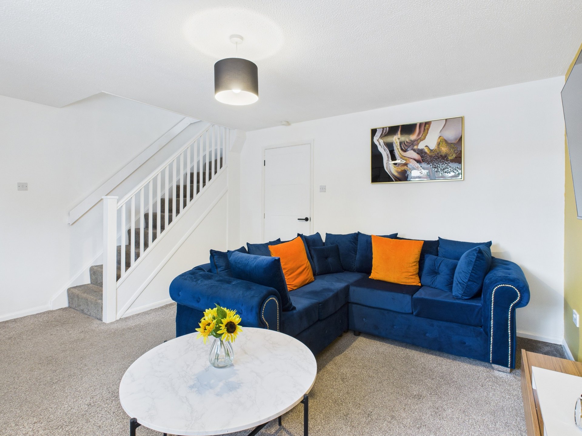 Living room with blue corner sofa, orange cushions, white round table, and staircase