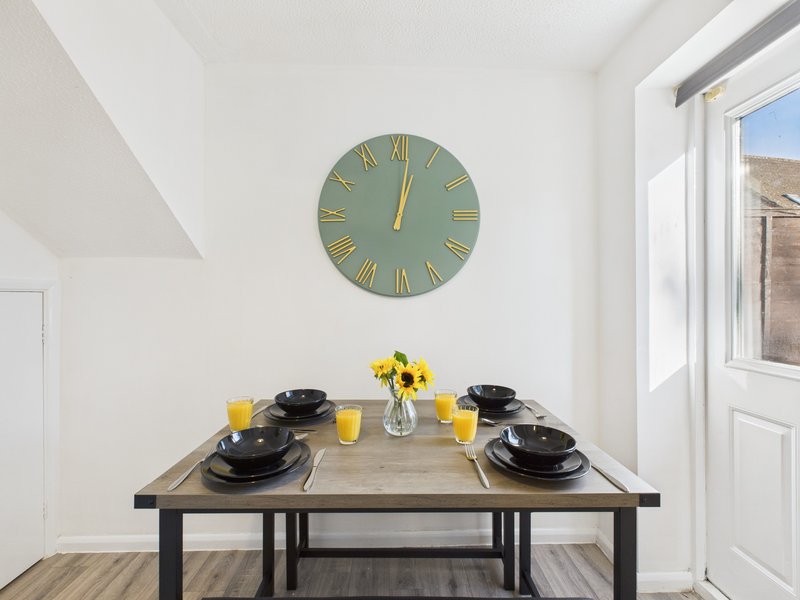 Dining table set for two with black plates, yellow flowers, and wall clock above