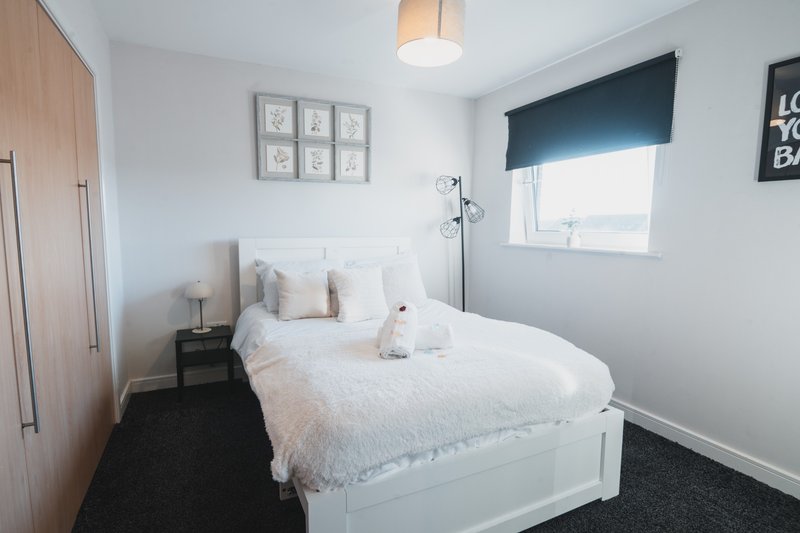 Modern bedroom with white double bed, wooden wardrobe, dark blue window blind and framed wall art