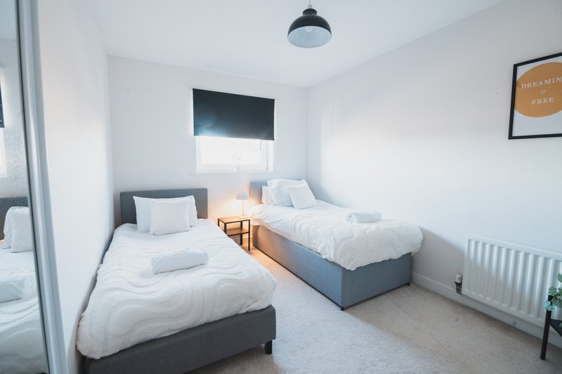 Bright twin bedroom with two single beds, white bedding, window with blind and wall-mounted lamp