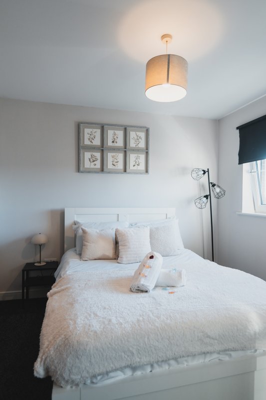 Bright bedroom with double bed, pendant ceiling light, framed wall art, and bedside table