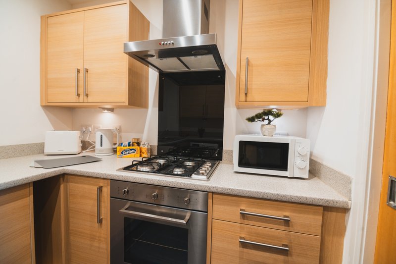 Modern kitchen with wooden cabinets, gas hob, black range hood and white microwave