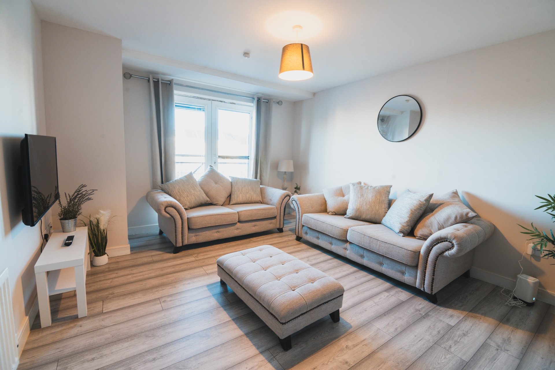 Bright living room with two beige sofas, ottoman, wooden flooring and large windows