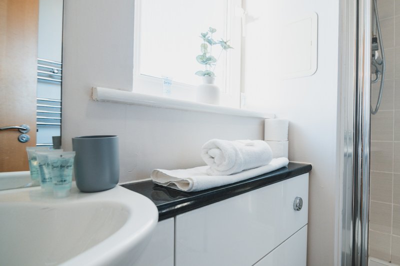 Clean bathroom with white sink, black vanity, rolled towels and shower enclosure
