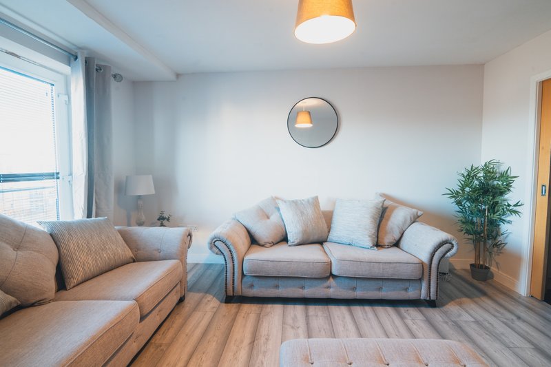 Bright living room with beige sofa, armchair, wooden floor and wall clock