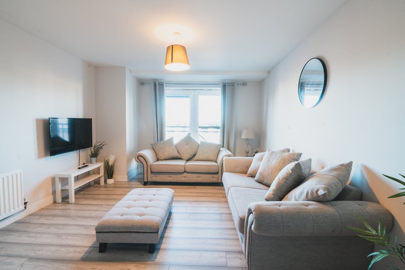 Bright living room with two sofas, ottoman, TV, wooden floor and large windows