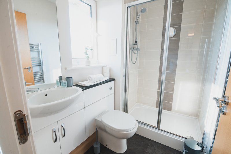 Modern bathroom with white vanity, toilet, shower enclosure and dark floor