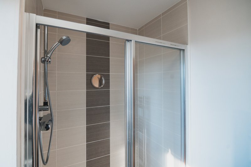 Modern bathroom shower enclosure with glass doors, chrome fixtures and beige tile walls