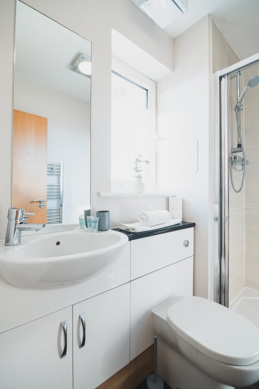 Modern bathroom with white sink, vanity storage, mirror, toilet and shower enclosure