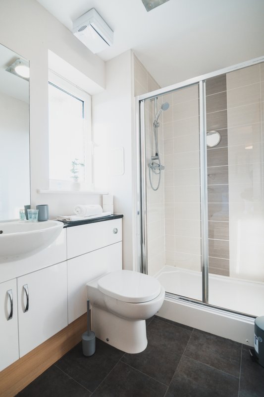 Modern bathroom with white vanity, toilet, shower enclosure and dark floor tiles