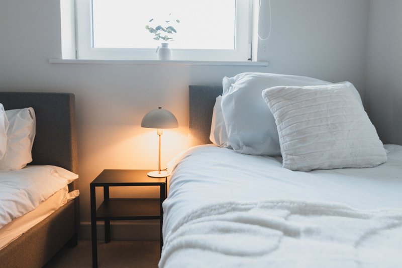 Bright bedroom with two single beds, white bedding, bedside lamp and window
