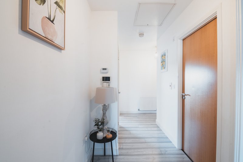 Bright hallway with wooden doors, small side table with plant, and framed botanical artwork
