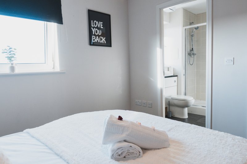 Bright bedroom with white bed, ensuite bathroom visible, window with blue blind