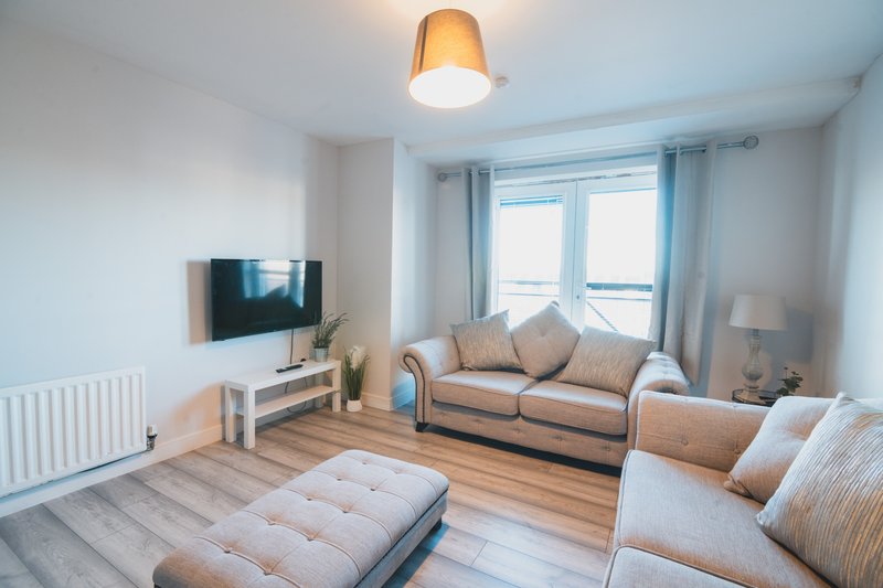 Bright modern living room with beige sofa, armchair, wooden floor and wall-mounted TV