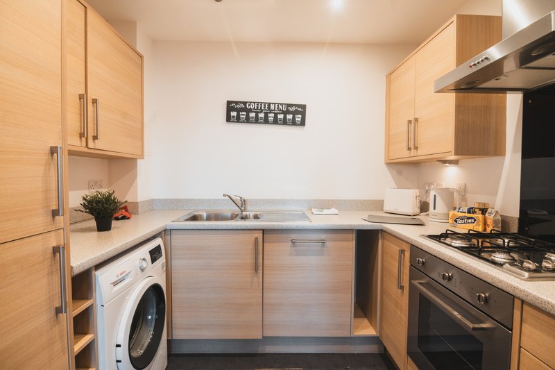 Modern kitchen with wooden cabinets, stainless steel appliances, washing machine and gas hob