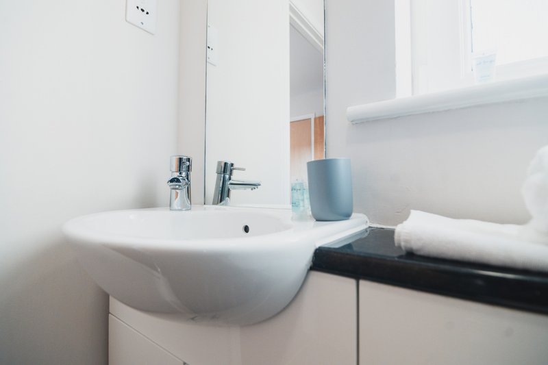 Clean modern bathroom with white sink, chrome tap, mirror, and bathroom accessories