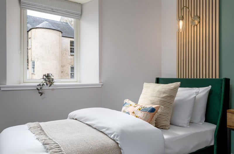 Modern bedroom with double bed, green headboard, striped curtains and window view