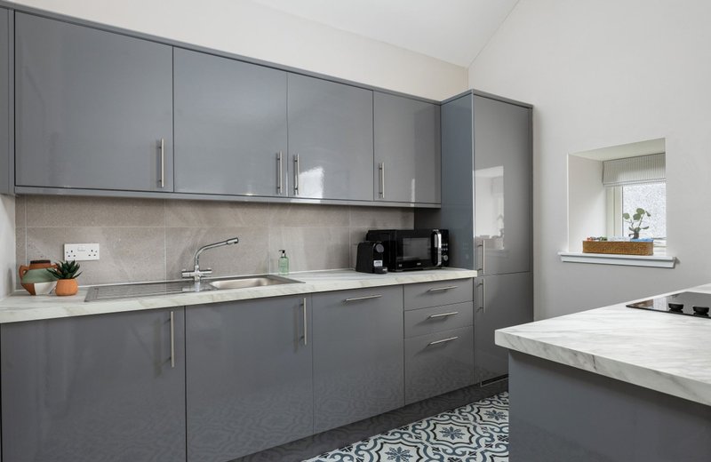 Modern kitchen with grey cabinetry, white countertops, sink, and black appliances