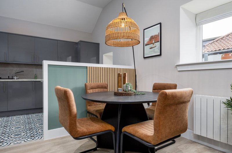 Modern dining area with round black table, tan leather chairs, woven pendant lamp and kitchen in background